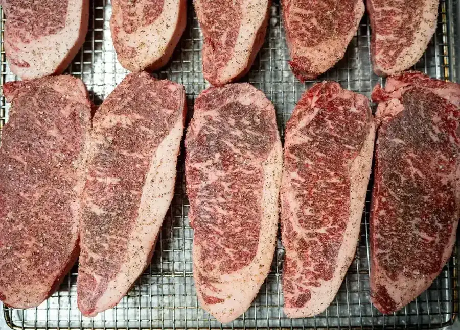 Seasoned steaks laid out on a rack in the catering kitchen ahead of a booked event