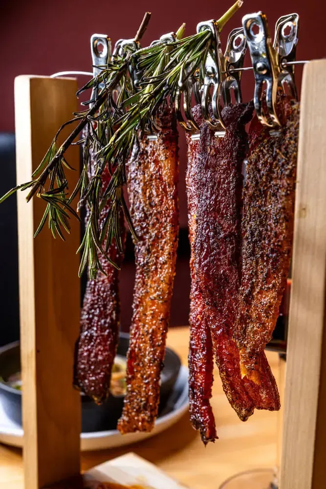 Glazed pork belly strips hung on a wooden appetizer rack. Catering in Druid Hill Park, Baltimore.