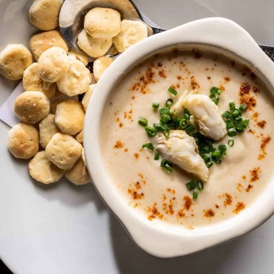 Bowl of Maryland cream of crab soup topped with lump crab and scallions, served with warm rolls