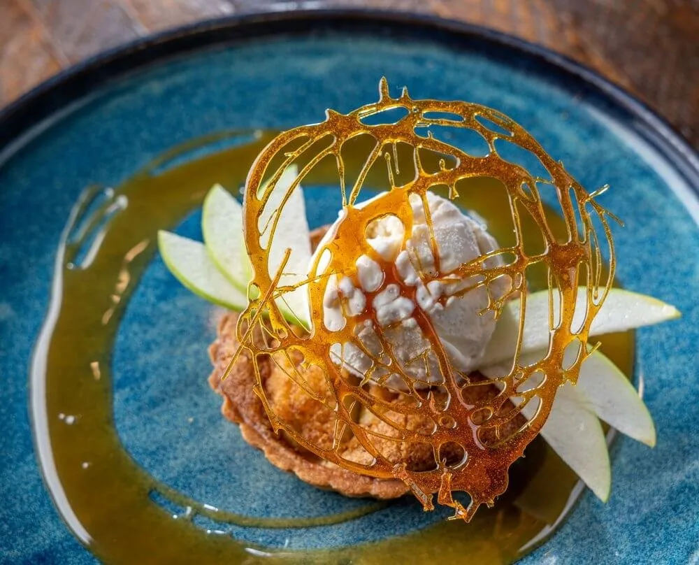 Plated dessert tasting course with a caramel sugar cage, ice cream and apple slices on a blue ceramic plate
