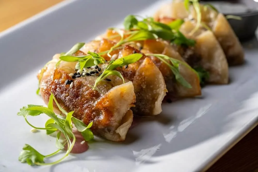 Plated dumpling tasting course with pea shoots and sauce on a long white ceramic plate