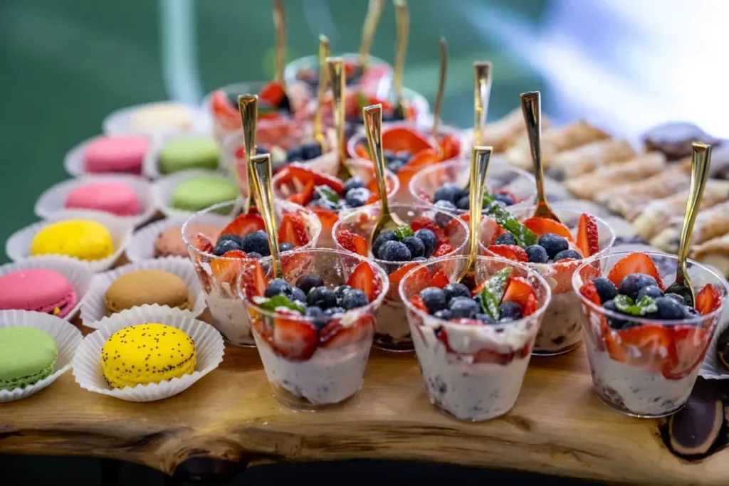 Graduation party dessert display with berry parfait cups, macarons, and pastries on a wood table
