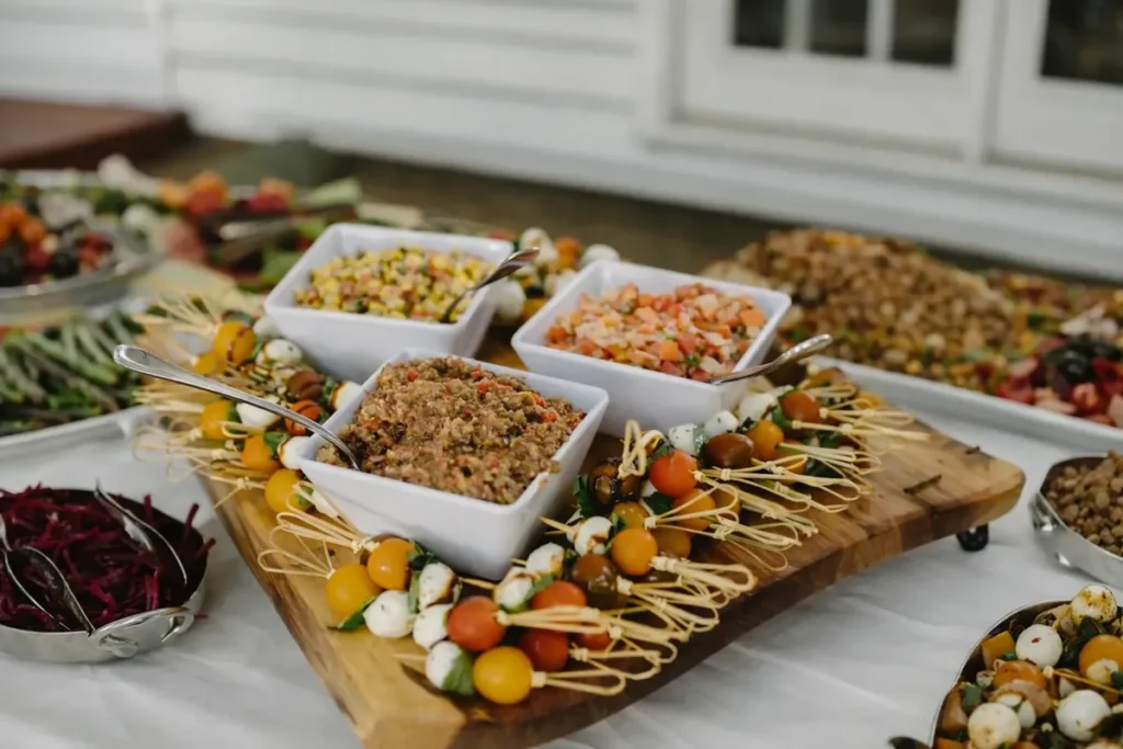 Catered grazing station with fresh salads, dips, and skewers arranged on a wooden serving board