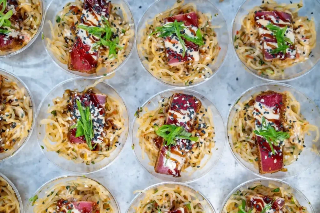 Rows of individually plated seared tuna appetizer cups prepared for a kosher-style catered event