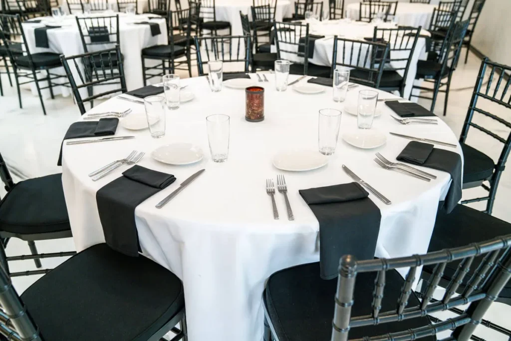 Round banquet table set with white linen, black napkins and full flatware for a catered wedding reception