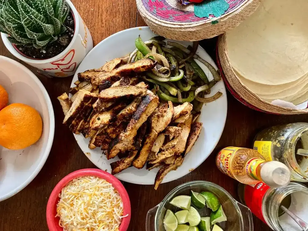 Chicken fajita spread with tortillas, cheese and limes on a table
