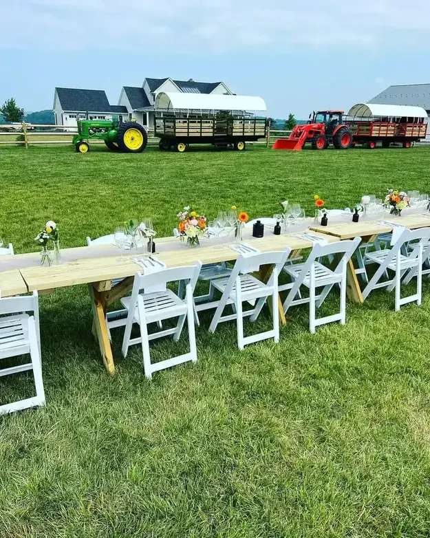 Long outdoor dining table with white chairs set on a lawn for a catered event in Baltimore